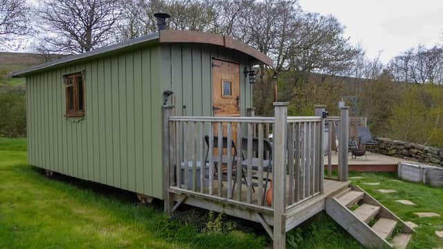 Green cabin with wooden deck, steps, and outdoor seating surrounded by grassy landscape and trees in Fryup, Yorkshire.