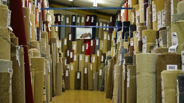 A wide aisle lined with rolls of carpets in various colors and textures, labeled for sale in a carpet store.