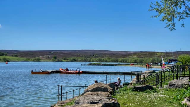 Calm waters of Scaling Dam with boats docked, lush greenery, and a clear blue sky in North Yorkshire.