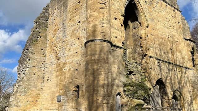 Knaresborough Castle ruins with stone walls, archway, and benches under a partly cloudy sky.