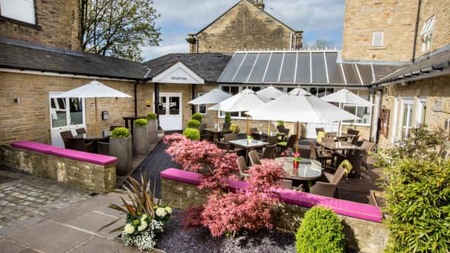Charming outdoor seating area at Herriots Hotel, featuring umbrellas, plants, and a pink bench in a picturesque setting.