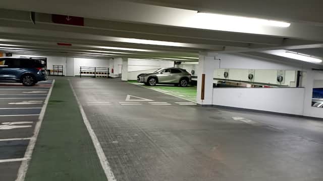 Empty car park with parked cars, green and white lines marking spaces, and overhead lighting illuminating the area.