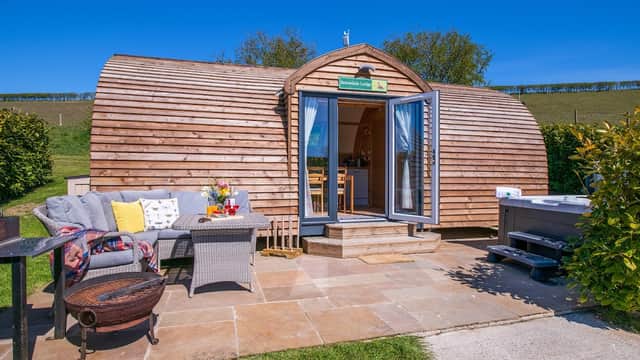 Charming wooden glamping pod with patio seating, surrounded by greenery under a clear blue sky in Folkton, Yorkshire.