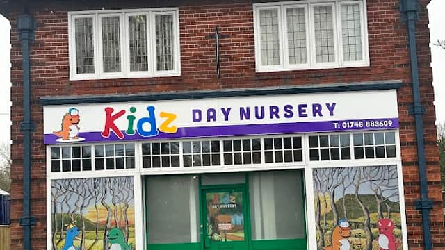 Brightly colored nursery sign with cartoon animals, large windows, and a green door in a brick building.