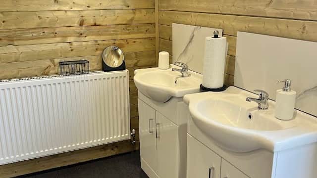 Modern bathroom with two sinks, wooden walls, a radiator, and natural light from a window.