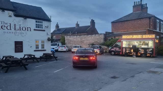 The Red Lion bar with outdoor seating, cars parked, and a food truck in the evening light.