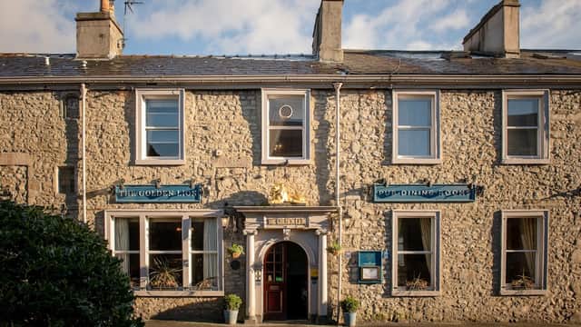 Charming stone building with a golden lion sign, blue window frames, and a welcoming entrance in Settle, Yorkshire.