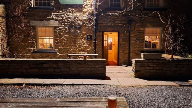 Redmire Village Pub with stone exterior, warm lighting, and a pint of beer on a wooden table in the foreground.
