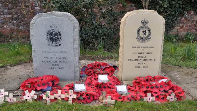 Two memorial stones for RAF and RCAF, surrounded by red poppies, in a garden setting with greenery in Burn, North Yorkshire.