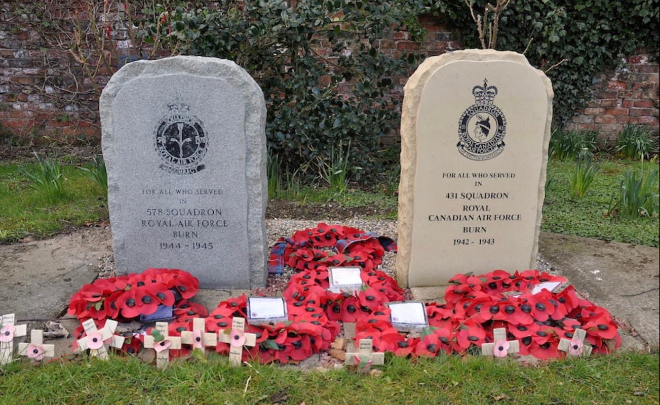 Two memorial stones for RAF and RCAF, surrounded by red poppies, in a garden setting with greenery in Burn, North Yorkshire.