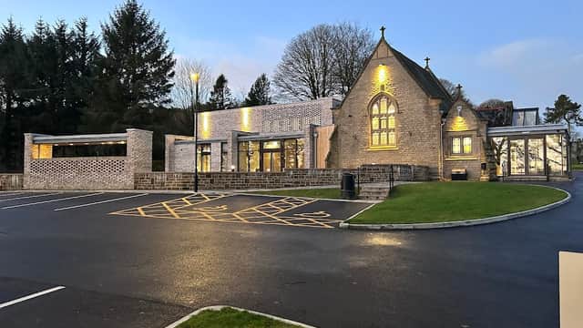 Modern stone building with large windows, surrounded by trees and a paved car park in Oakworth Cemetery, Yorkshire.