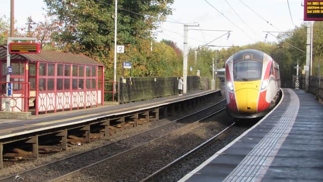 Train approaching Outwood Station, with a red and white shelter and platform signs visible. Trees in the background.