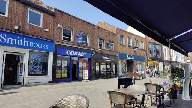 Shops line a sunny street in Beverley, with outdoor seating and people walking by.