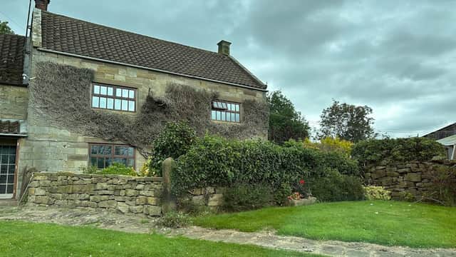 Stone cottage with ivy, surrounded by green grass and a stone wall, under a cloudy sky in Lealholm, Yorkshire.