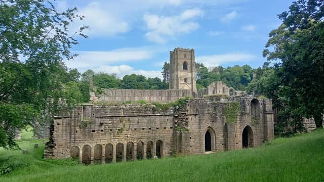 Ruins of Fountains Abbey surrounded by lush greenery under a blue sky with scattered clouds.