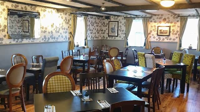 Cozy bar interior with wooden floors, tables, and patterned chairs, adorned with floral wallpaper and soft lighting.