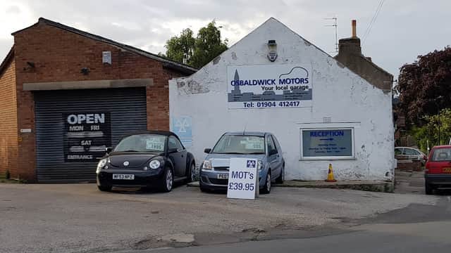 Osbaldwick Motors Ltd garage with two cars parked outside and a sign displaying MOT prices and contact information.
