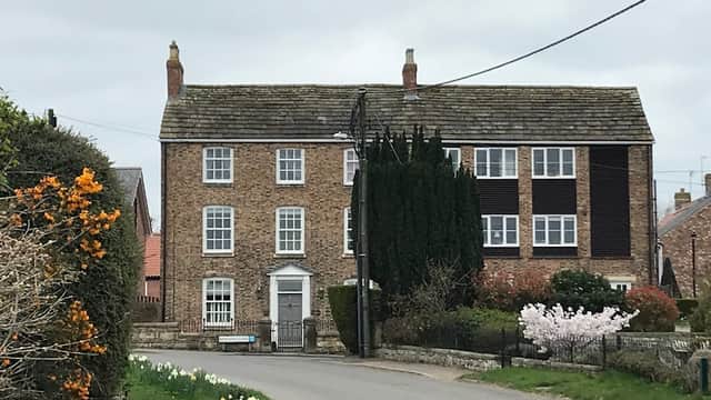 Brick building with multiple windows, surrounded by greenery and flowers, located on a quiet road in Bishop Monkton.