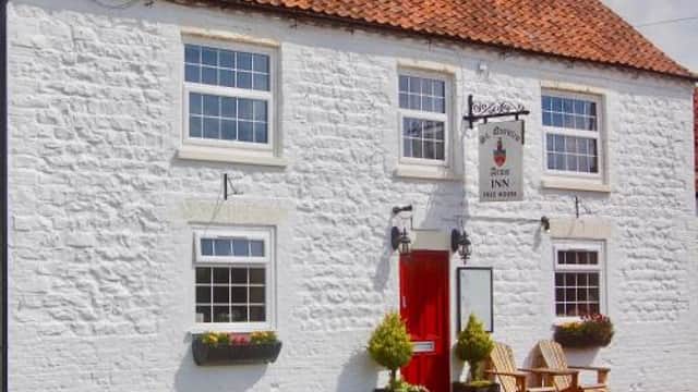 Whitewashed building with a red door, windows with flower boxes, and a sign hanging above the entrance.