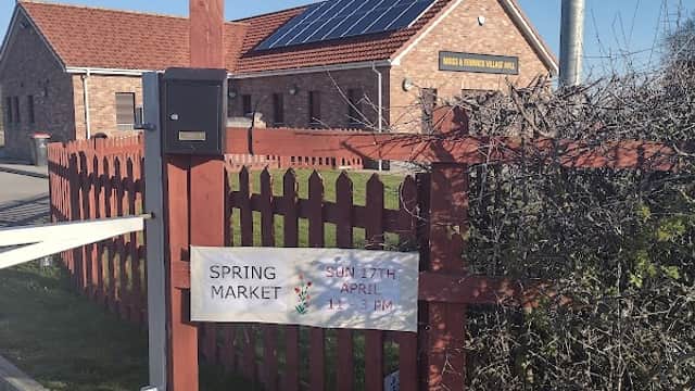 Moss and Fenwick village hall with solar panels, a wooden fence, and a sign for the Spring Market event.