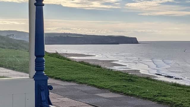 View from a seaside shelter overlooking the beach, cliffs, and calm sea under a cloudy sky in Whitby, Yorkshire.