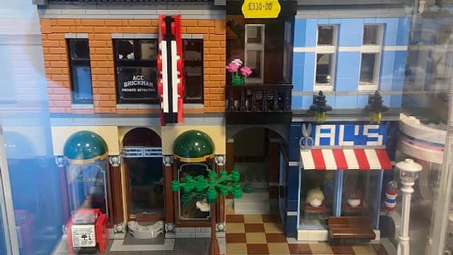 Toy shop display featuring detailed LEGO buildings, including a café and a barber shop, with colorful signage and trees.