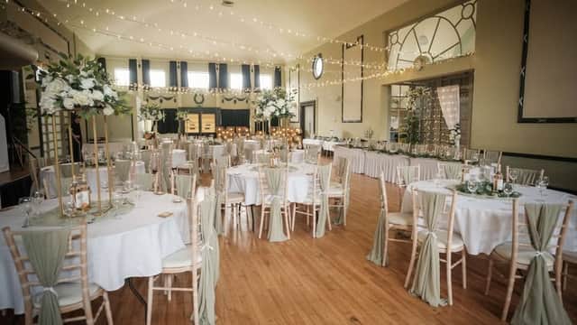 Elegant event space featuring round tables with white linens, greenery centerpieces, and twinkling string lights.