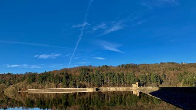Broomhead Reservoir surrounded by trees under a clear blue sky, reflecting in the calm water.