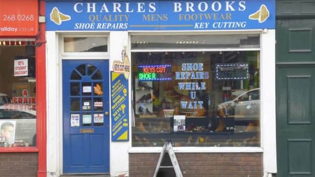 Blue storefront with "Charles Brooks" sign, display of shoes, and neon signs for shoe repairs and key cutting.