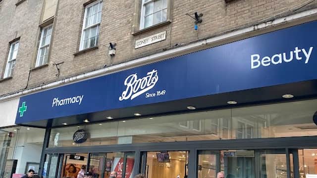 Boots store front featuring "Pharmacy" and "Beauty" signs, with shoppers and a child in a stroller outside.