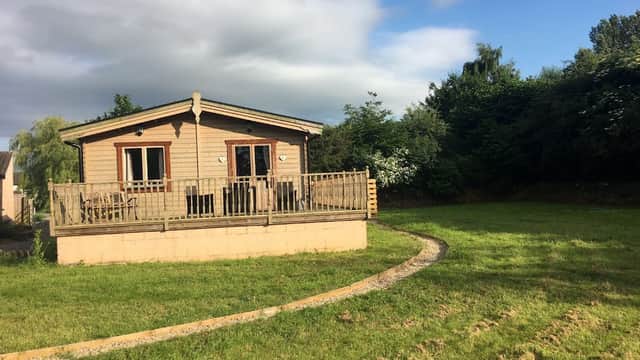 Wooden cabin with a deck, surrounded by green grass and trees under a partly cloudy sky in Seaton Ross, Yorkshire.