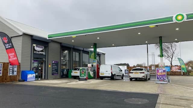 Grocers with a fuel station, featuring a BP sign, cars, and promotional banners in a cloudy setting.
