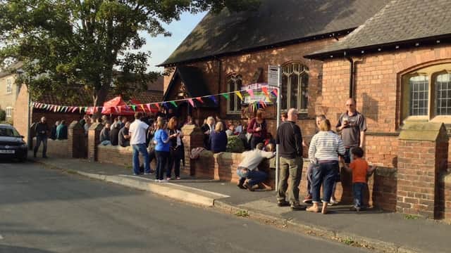 People gather outside Ulleskelf Village Hall, decorated with colorful bunting, enjoying a community event on a sunny day.