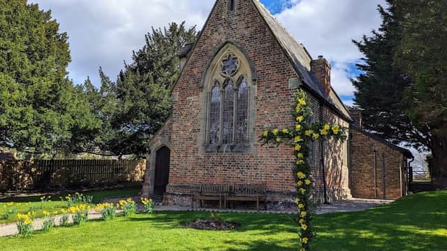 Minskip Village Hall features a brick building with stained glass windows, surrounded by trees and blooming daffodils.