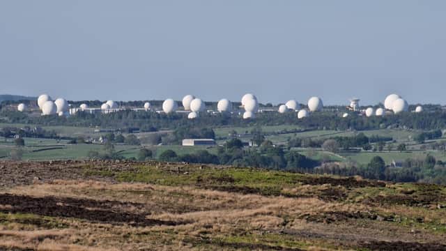 White radar domes scattered across a green landscape under a clear blue sky, with moorland in the foreground.