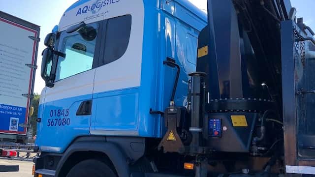 Blue and white truck with "AQ Logistics Ltd" branding, parked beside a large billboard in Ainderby Quernhow, Yorkshire.