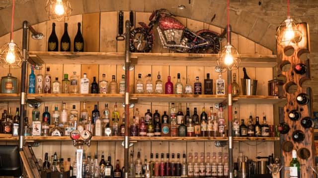 Wooden shelves filled with various bottles of spirits, a vintage motorcycle decoration, and pendant lights hanging above.
