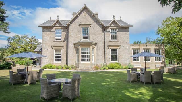 Elegant stone building surrounded by lush greenery, featuring outdoor seating with umbrellas in a picturesque setting.