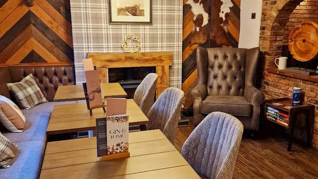 Cozy pub interior featuring wooden tables, plush chairs, and rustic decor with a fireplace and patterned walls.