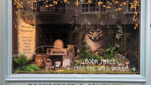Bookshop window display featuring a wolf, lion, and nature-themed decor with "Welcome to Rookscroft" sign.