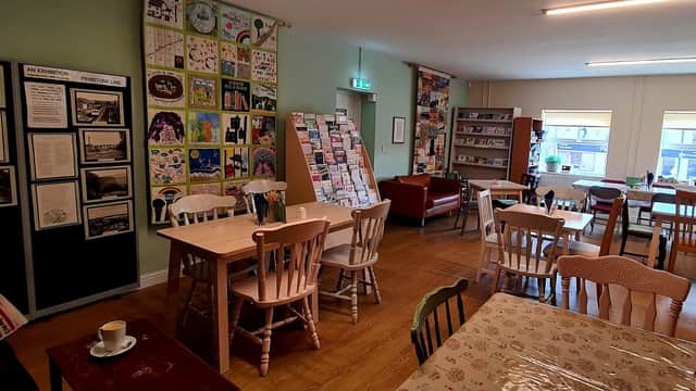 Cozy café interior with tables, chairs, art displays, and bookshelves in Denby Dale Community Library.