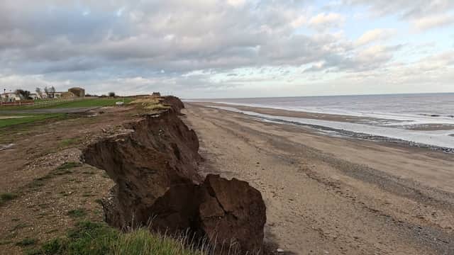 Eroded cliff edge overlooking a sandy beach with gentle waves and cloudy sky in Tunstall, Yorkshire.