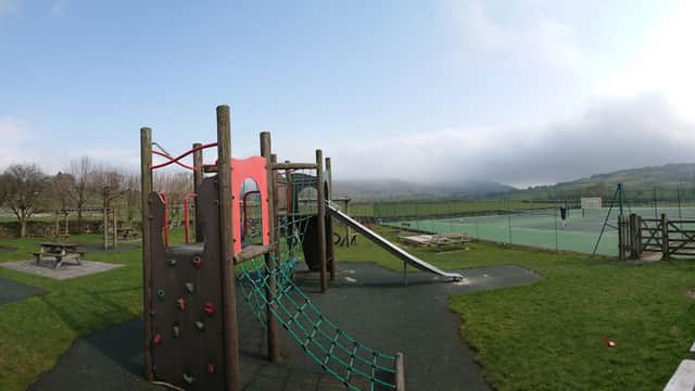 Colorful play equipment with a climbing frame and slide, surrounded by green grass and distant hills under a cloudy sky.
