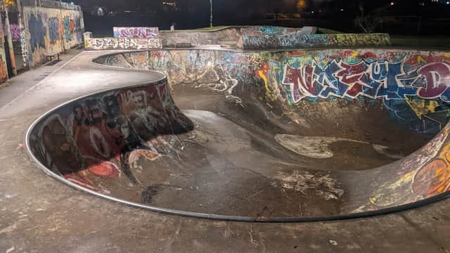 Skatepark with curved concrete bowls, vibrant graffiti on surfaces, and dim lighting in a night setting.