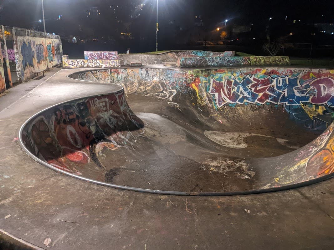 Skatepark with curved concrete bowls, vibrant graffiti on surfaces, and dim lighting in a night setting.