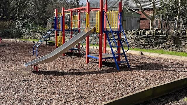 Colorful playground equipment with a slide, surrounded by wood chips and trees in Denby Dale, Yorkshire.