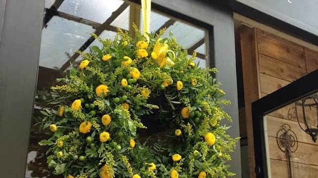 A vibrant yellow floral wreath with a bow, hanging on a shop door under a sign that reads "Helen James Harrogate."