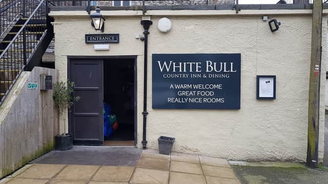 Entrance to The White Bull pub, featuring a sign with welcoming messages, stone walls, and a staircase in the background.