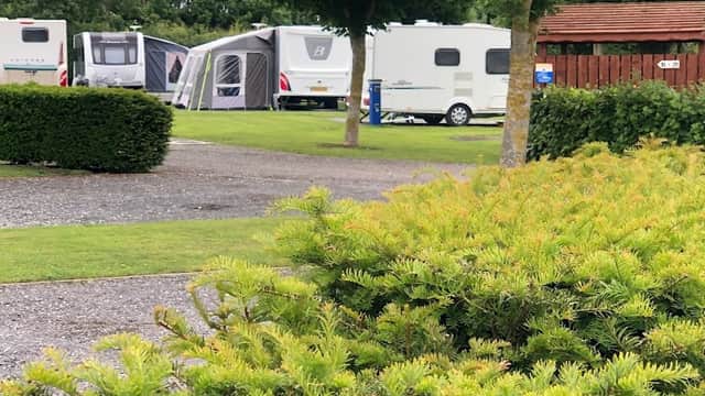 Lush green landscape with neatly trimmed bushes, caravans parked in the background, and trees lining the area.