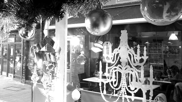 Decorative storefront with festive ornaments, a chandelier design, and reflections of a nearby restaurant in Wetherby.